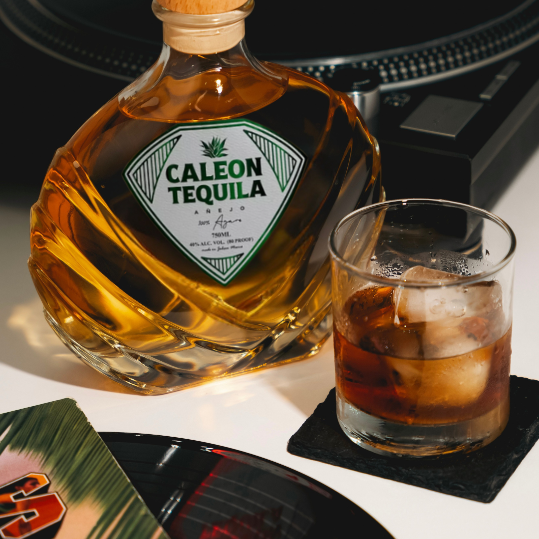 Caleon Tequila Añejo bottle next to a glass of tequila with ice and a record player in the background