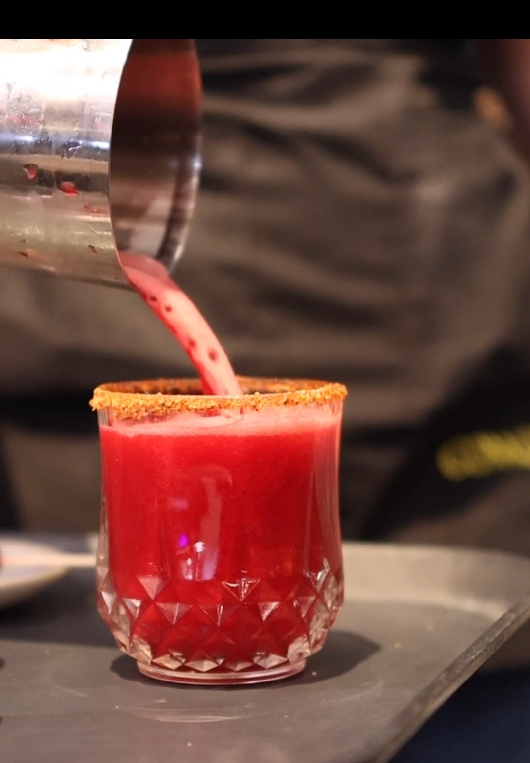 Watermelon red cocktail being poured into a glass with a sugared rim on a bar counter featuring Caleon Blanco Tequila